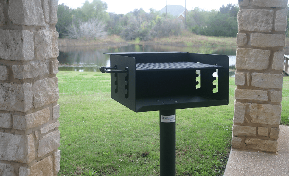Commercial park grill installed on a pedestal in an outdoor pavilion overlooking a lake, designed for durable public use in parks and recreational areas